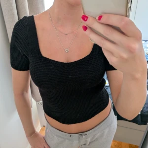 Svart ribbad stickad topp - Säljer en svart, ribbstickad topp med fyrkantig urringning och korta ärmar. Modellen är croppad och sitter tight, perfekt för dig som gillar en enkel men ändå snygg look. Materialet är mjukt och stretchigt stickat tyg.