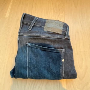 Replay Anbass Hyperflex mörkblå jeans - Snygga mörkblå Replay Anbass Hyperflex jeans i klassisk femficksmodell. Jeansen har en slim passform och är tillverkade i mjukt denimtyg med stretch. Perfekta för dig som gillar en stilren look med diskreta detaljer och bekväm känsla.