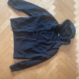 Svart hoodie från Polo Ralph Lauren - Svart hoodie från Polo Ralph Lauren med dragkedja och huva. Klassisk design med två fickor framtill och den ikoniska röda loggan broderad på bröstet. Tillverkad i mjuk bomull, perfekt för chill dagar eller när du vill ha en enkel och snygg look.