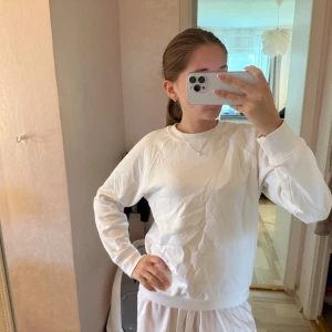 Vit basic sweatshirt i bomull - Enkel och stilren vit sweatshirt med rund halsringning och långa ärmar. Tröjan är i mjuk bomull och har ribbade muddar vid ärmslut och nederkant. Perfekt för en clean och avslappnad look.