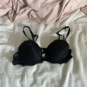 Svart spets-bh med vaddering - Snygg svart bh med spetsdetaljer och vadderade kupor. Axelbanden är justerbara och bh:n har en feminin look med fina spetskanter. Perfekt för dig som gillar en klassisk och stilren stil.