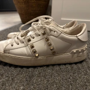 Valentino Rockstud vita sneakers - Säljer ett par vita Valentino Rockstud sneakers i skinn med nitar i guld längs sidorna och på hälen. Skorna är välanvända som man kan se och har dekretet som syns på bilderna därav är priset lågt
