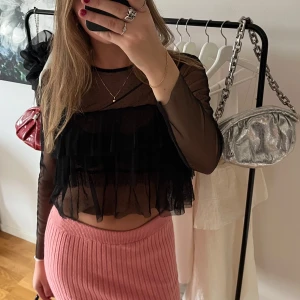Svart mesh blus med volanger - Säljer en svart transparent meshblus med långa ärmar och volangdetaljer framtill. Blusen är croppad och har små prickar i tyget för extra detalj. 