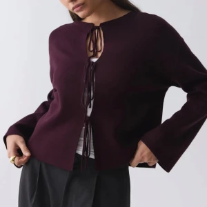 Vinröd kofta med snörning från Gina Tricot - Vinröd kofta från Gina Tricot med trendig snörning framtill. Modellen är croppad med långa ärmar och rund halsringning. Koftan är stickad och har en loose passform, perfekt att slänga över en topp för en chill look.