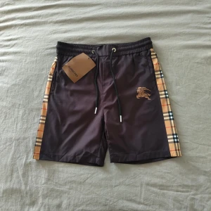 Burberry shorts - Snygga Burberry shorts i marinblå med klassiska rutor på sidorna. Märkta som XL men passar mer som M/L enligt min bedömning. Helt oanvända och i nyskick.