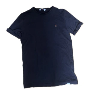 Svart t-shirt från Les Deux - Svart t-shirt från Les Deux med diskret broderad II-logga på bröstet. Klassisk rund hals och korta ärmar med uppvik. Tillverkad i mjuk bomull som känns skön mot huden. Perfekt för dig som gillar stilrena och enkla plagg.