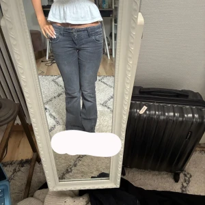 Grå bootcut jeans med fickdetaljer - Säljer ett par grå jeans med bootcut-modell och snygga fickor med lock och knapp bak. Jeansen har låg midja och klassisk femficksdesign. Perfekta för dig som gillar en retro vibe och vill ha ett par jeans som sticker ut lite extra. Väldigt låga.