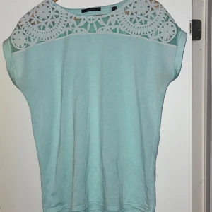 Mintgrön top  med spets från Esprit - Superfin mintgrön top från Esprit med korta ärmar och snygg spetsdetalj över axlarna och övre bröstet. Blusen har en avslappnad passform och är gjord i mjuk bomull, 