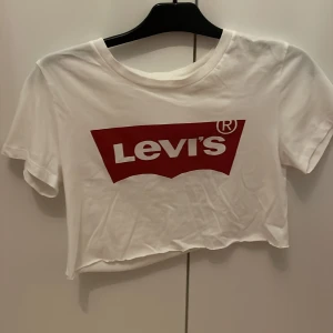 Vit t-shirt från Levi's - Säljer en vit croppad t-shirt från Levi's med den klassiska röda loggan framtill. Den är klippt där nere så den blev kortare men annars är den i väldig fint skick och väldigt snygg😍