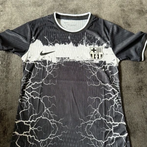 FC Barcelona x Nike svart/vit fotbollströja - Snygg FC Barcelona fotbollströja från Nike i svart och vitt med elektriskt blixtmönster över hela tröjan. Helt ny, Storlek S
