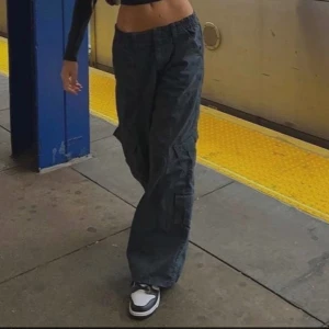 Grå cargopants från Urban outfitters - Säljer ett par svarta cargopants med bred passform och flera fickor på sidorna. Byxorna har elastisk midja och är perfekta för en avslappnad streetstyle-look. Materialet känns slitstarkt och de är riktigt bekväma att bära.