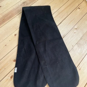 Svart ullhalsduk - En klassisk svart halsduk i mjuk ull. Enkel och stilren design utan mönster, perfekt att slänga över axlarna när det är kallt ute. Halsduken är lång och har rundade kanter för en clean look.