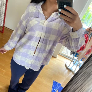 Ljuslila och vit rutig skjorta - Superfin skjorta i ljuslila och vitt rutigt mönster. Skjortan har klassisk krage, knäppning framtill och långa ärmar med manschett. Perfekt för en chill och avslappnad stil. Materialet känns lätt och luftigt.