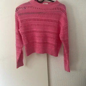 Rosa stickad tröja från H&M - Säljer en rosa stickad tröja från H&M i storlek 146/152. Tröjan har ett snyggt hålmönster, ribbade muddar och är långärmad. Perfekt för dig som vill ha en färgglad och trendig look med en lite croppad passform.