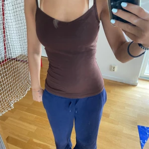 Brun tight linnetopp med smala axelband - Säljer en brun, tight linnetopp med smala axelband och v-ringad hals. Perfekt för dig som gillar en enkel och stilren look. Toppen är ärmlös och har en figurnära passform som framhäver siluetten.