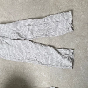 Randiga linnebyxor från Gina Tricot - Luftiga och bekväma linnebyxor från Gina Tricot i ljusgrått med vita ränder. Byxorna har rak passform, elastisk midja med snörning och är perfekta för varma dagar. Snyggt avslappnad stil som funkar till allt.