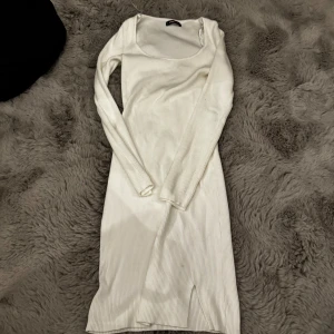 Vit ribbad långärmad klänning - Snygg vit ribbad klänning med lång ärm och rundad urringning. Modellen är kroppsnära och har en liten slits nertill. Perfekt för dig som gillar stilrena och enkla plagg med en modern touch. Från New Yorker i storlek L