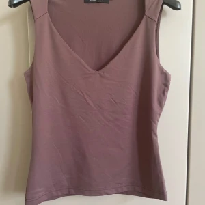  ärmlös linnetopp med v-ringning - En stilren linnetopp med v-ringad hals och ärmlös design. Toppen har en enkel och clean look, perfekt att matcha med jeans eller kjol. Mjuk och skön i materialet, passar för både chill och mer uppklädda tillfällen.