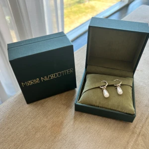 Maria Nilsdotter örhängen med pärlor - LÄS INNAN KÖP: Snygga örhängen från Maria Nilsdotter i silver med droppformade vita pärlor. Nypris för ett par är 3990kr och för ett örhänge ligger nypris på 1995kr. Mitt pris för båda örhängena (par) ligger på 2900 och om du vill köpa endast ett är de 1449. Box medföljer 