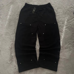 BoohooMAN Wide Leg Carpenter Joggers - Strl L - Säljer ett par helt nya svarta Wide Leg Carpenter Joggers från boohooMAN  Size - L   Aldrig använda, prislappen sitter fortfarande kvar.  Loose fit med breda ben och cargo/carptenter-detaljer – perfekt för dig som gillar streetwear med funktionell look. Mjuk bomullsblandning och resår i midjan för extra komfort. Säljer pga fel storlek.  📐 Mått finns på bilder  📦 Fraktar samma/nästa dag  📸 Fler bilder vid behov ✅ Nypris 300kr