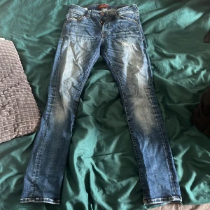 Slim Glenn blå jeans i storlek 27/30 - Snygga blå jeans från Slim Glenn i storlek 27/30. Modellen är slim fit med klassisk femficksdesign och slitna detaljer framtill. Jeansen har en något ljusare tvätt på låren och knän, vilket ger en cool, använd look.