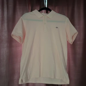 Ljusrosa pikétröja från GANT - Snygg ljusrosa pikétröja från GANT med klassisk krage och knappar framtill. Tröjan har korta ärmar och är tillverkad i mjuk bomull. Broderad GANT-logga på bröstet ger en stilren look. Perfekt nu för sommaren. Nypris: Ca 600kr