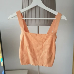 Persikofärgad ribbad linnetopp Zara - Superfin persikofärgad linnetopp från Zara med breda axelband och ribbad struktur. Toppen är croppad och har en fyrkantig halsringning, perfekt för varma dagar.