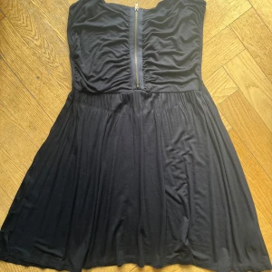 Svart axelbandslös klänning Gina Tricot - Svart axelbandslös kortklänning från Gina Tricot med snygg dragkedja framtill. Klänningen har en lätt utställd kjol och är tillverkad i mjuk viskosblandning med stretch. Perfekt för dig som gillar enkel men stilren look.