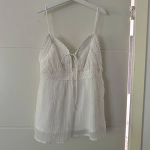 Vit linnetop  - Superfin vit linnetopp med tunna axelband och spetsdetaljer upptill. Toppen har v-ringning och knytning framtill. Perfekt för varma dagar eller sommarhäng. Aldrig använd.