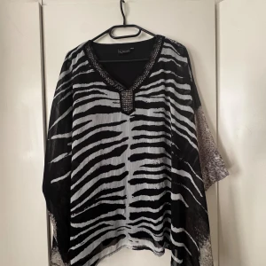 Zebramönstrad blus från Cellbes - Snygg och luftig blus från Cellbes med svartvitt zebramönster och v-ringning med glittriga detaljer. Ärmarna har ett genomskinligt tyg.