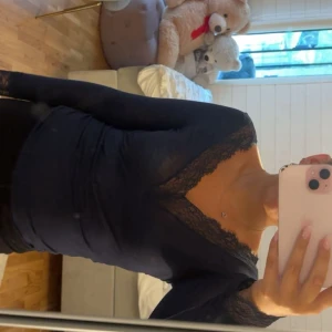 Mörkblå långärmad topp med spets - Snygg mörkblå långärmad topp med v-ringning och spetsdetaljer vid halsringning och ärmslut. Figurnära passform som sitter riktigt bra och ger en stilren look. Perfekt att matcha med jeans eller kjol för en trendig outfit.