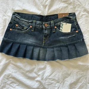 Jeanskjol från Peak Performance - Mörkblå jeanskjol från Peak Performance med volanger och klassiska fickor fram och bak. Kjolen har synliga sömmar i gult och en cool, kort modell som ger en trendig vibe. Midjemått 38 cm rakt över. Hör av dig vid funderingar!🌟🌟