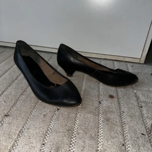 Svarta klassiska pumps i skinn - Stilrena svarta pumps med låg klack och rund tå. Skorna är tillverkade i skinn och har en tidlös design som passar till många olika outfits. Perfekta för dig som gillar en enkel och elegant look.