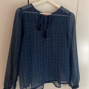 mörkblå långärmad blus - supervacker långärmad blus med ett mycket fint mönster och lätt tyg!! har en snöresdetalj vid halsen med fransar på. saknas en knapp på en av ärmarna, annars mycket bra skick då den endast är använd ett fåtal gånger ❣️