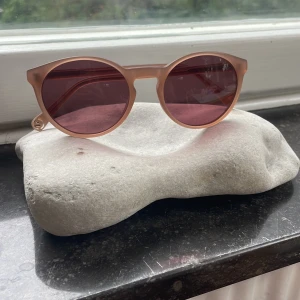 Beige runda solglasögon från Elite - Snygga runda solglasögon från Elite med beige transparent båge och mörkt rosatonade glas. Modellen är ELT1709 och har en stilren, modern look som passar perfekt till sommaren. Lätta och bekväma att bära, med cool detalj på skalmen.