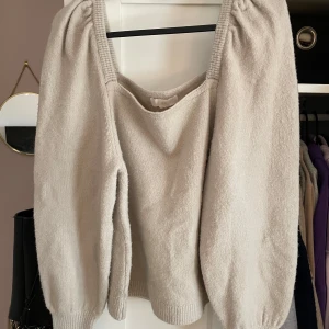 Beige stickad tröja med puffärm och urringning!  - Superfin beige stickad tröja med bred, fyrkantig ringning och puffiga långärmar. Tröjan har ribbade muddar vid ärmslut och nederkant. (Porto tillkommer) 