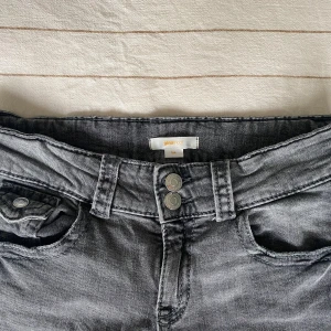 Grå bootcut jeans från Gina Tricot young - Snygga grå jeans från Gina Tricot i bootcut-modell. Jeansen har låg midja, klassiska fem fickor och dubbla knappar framtill. Tillverkade i mjukt denimtyg med lätt tvättad look. Perfekta för dig som gillar en avslappnad men trendig stil.