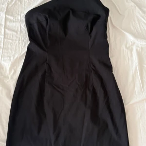 Svart one shoulder kort klänning - Snygg svart kort klänning från NAKD med one shoulder-design. Klänningen har en tight passform och ärmlös stil som ger en clean och modern look. Perfekt för dig som gillar minimalistiska, asymmetriska och stilrena plagg.