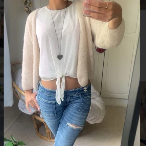 Vit blus med knyt och prickar - Superfin vit blus från Lindex med diskreta prickar i tyget och transparenta, vida ärmar. Blusen har knyt framtill som ger en snygg croppad look. Perfekt till jeans eller kjol för en fräsch och somrig stil.