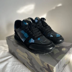 Valentino rockrunners strl 41 men passar 42 - Snygga Valentino Garavani Rockrunner sneakers i svart och blått med coolt camouflagemönster. Skorna har svarta snören, rund tå och detaljer i skinn och mocka. Perfekta för dig som vill sticka ut med exklusiva och trendiga sneakers.