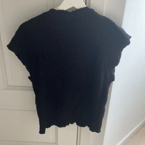 Svart stickad topp från Zara - Svart stickad topp från Zara med grov struktur och korta ärmar. Modellen är boxig och har en lite lös passform, perfekt för lager-på-lager eller som den är. Materialet är mjukt och känns skönt mot huden. Enkel att styla till både jeans och kjol.