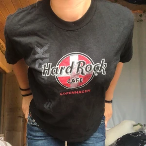 Svart Hard Rock Cafe t-shirt Köpenhamn - Svart t-shirt från Hard Rock Cafe med stort tryck på bröstet i vitt och rött med texten 'Copenhagen'. Klassisk passform, rund hals och korta ärmar. Tillverkad i 100% bomull, perfekt för dig som gillar ikoniska bandtröjor och streetstyle.