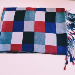 Rutig halsduk i blått, rött och vitt - Snygg halsduk med rutigt mönster i blått, rött, svart och vitt. Långa fransar i ändarna ger extra stilpoäng. Perfekt accessoar för att lyfta din outfit med lite färg och mönster. Mjuk och lätt, enkel att slänga över axlarna.  Helt skick dock noppror