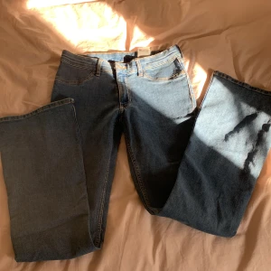 Blå flared jeans från H&M - Snygga blå jeans från H&M med flared ben och låg midja. Klassisk femficksmodell med justerbar midja och orangea sömmar. Materialet är en mix av bomull, polyester och elastan för en bekväm passform.