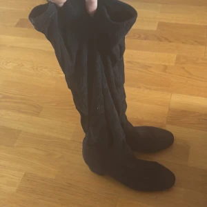 Svarta mockastövlar med låg klack - Snygga svarta stövlar i mjuk mocka liknande material med rund tå och låg klack. De är höga och har en klassisk, stilren look som passar perfekt till kjol eller jeans. Materialet som ger en lyxig känsla och de är lätta att matcha med olika outfits.