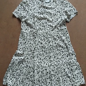 Härlig Sommarklänning - Vit klänning med svarta prickar, kortärmad och går till knäna. Knäpps med en knapp i nacken. Helt i viskos, jätteskönt tyg. Från Vila i storlek 38, nästan helt ny så skicket är toppen. Den är verkligen söt!
