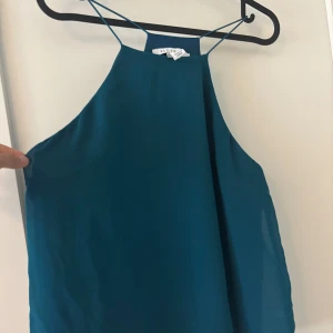 Turkos linnetopp med tunna axelband - Snygg turkos linnetopp från NLY Trend med tunna axelband och hög halsringning. Toppen har en enkel och stilren design som ger en fräsch look. Perfekt för varma dagar eller när du vill ha något lätt och luftigt.