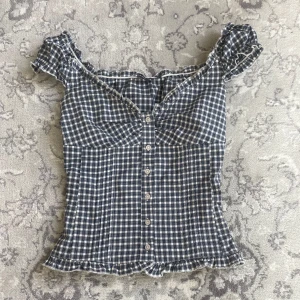 Rutig blus från Brandy Melville - Supersöt rutig blus från Brandy Melville i marinblått och vitt. Blusen har knappar framtill, volangkant vid axlar och nederkant.💞