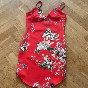 Röd blommig kortklänning med smala axelband - Superfin röd kortklänning från H&M med blommigt mönster i vitt, grönt och rosa. Klänningen har smala axelband, v-ringning och figurnära passform. Perfekt för sommarens alla tillfällen och ger en färgstark look.