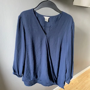 Mörkblå omlottblus - Säljer en mörkblå omlottblus från Lindex med  långa ärmar. Har använt 1 gång. 